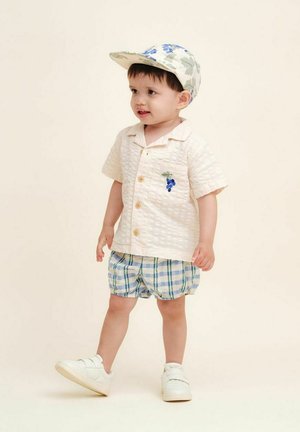 Kortærmet cremebluse med struktureret stof og druebroderi, parret med blå og grønternet shorts og hvide sneakers. Blomsterkasket.