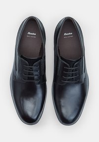 Scarpe formali in pelle nera con lacci, di marca "Bata," viste dall'alto su uno sfondo bianco uniforme.