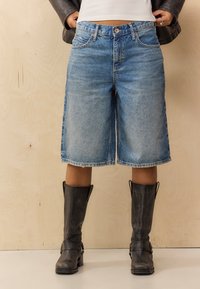 Shorts en denim bleu clair avec un ourlet effiloché et un design classique à cinq poches. Associés à des bottes en cuir noir hauteur genoux.