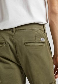 Olivgröna shorts i bomullsblandning med en mjuk textur, med bakfickor och en liten varumärkesetikett på högra sidan.