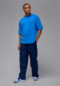 Sininen lyhythihainen t-paita mustalla logolla, tummansiniset cargo-housut ja sinivalkoiset tennarit. Sileä kangas, rento istuvuus, ilman kuvioita.