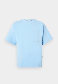 T-shirt de algodão azul-claro com mangas curtas, decote redondo e um bolso no lado esquerdo do peito. Apresenta botões de metal em destaque no bolso.