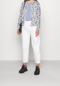 Bomberka w czarno-białe wzory, jasnoniebieska koszulka, białe jeansy z wysokim stanem i czarne trampki z teksturowanymi akcentami.