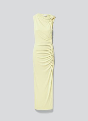 Vestido largo sin mangas de color amarillo pálido con detalle fruncido en el lateral y tela recogida asegurada por un pequeño anillo en un hombro.