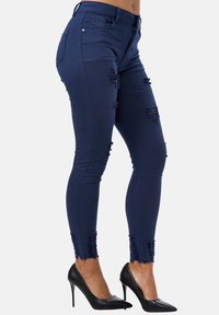 Jeans skinny azul marino con detalle desgastado, dobladillos desflecados y una cintura de altura media, combinados con zapatos de tacón negro.
