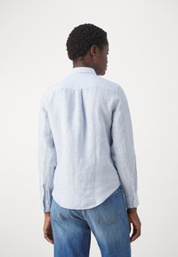 Jasnoniebieska lniana koszula z długimi rękawami, ze spiczastym kołnierzykiem i zaokrąglonym dołem, z guzikami na mankietach i teksturowanym materiałem.