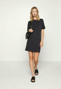 Vestido azul-marinho de manga curta com um corte solto, combinado com sandálias pretas de encaixe e uma pequena bolsa preta. Textura de tecido suave.