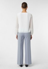 Biała bluzka z długimi, przezroczystymi rękawami z wzorem w kratkę na mankietach, zestawiona z jasnoniebieskimi spodniami o szerokich nogawkach.