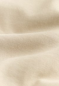 Tissu tricoté beige clair présentant des coutures fines et régulières ainsi qu'une texture douce avec des plis et des ombres délicats.