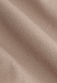 Tissu beige avec une texture lisse et étroitement tissée, des plis doux créant des ombres et des reflets délicats.