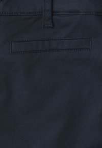 Close-up of dark fabric with a horizontal welt pocket and a belt loop above the pocket, showing detailed stitching.