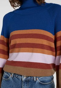 Sinivalkoinen ja ruskea raidallinen pooloneule, jossa on sävyjä viininpunaista, vaaleanpunaista, oranssia ja ruskeaa sekä pehmeä, teksturoitu pinta.