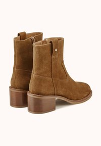 Bottines en daim marron à bout rond, fermeture éclair, et talon en bois empilé. Elles comportent un panneau latéral pour un enfilage facile.