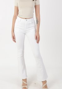 White flared jeans with a high waist, made of denim, featuring five pockets and a button and zipper closure. Smooth, structured texture.
