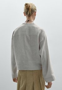 Sweatshirt en velours côtelé gris clair, coupe ample, manches larges, surface texturée, avec une couture dans le dos, porté par-dessus une jupe beige.