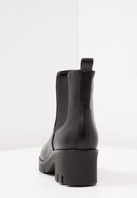 Czarne skórzane botki za kostkę z elastycznymi panelami bocznymi, okrągłym noskiem i masywnym obcasem. Teksturowana powierzchnia, pętla z tyłu.