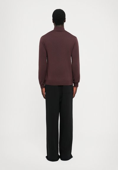 Pull en maille bordeaux avec un col montant, des manches longues et des poignets côtelés, associé à un pantalon noir à jambe large. Vue arrière.