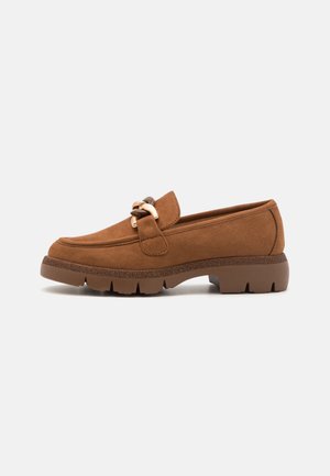 Mocassins en daim marron avec un accent décoratif en chaîne dorée, dotés d'une semelle en caoutchouc texturée et d'un design à bout rond.