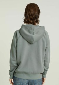 Mikina s kapucí ve světle zelené barvě, vyrobená z měkké látky. Disponuje raglánovými rukávy a žebrovanými manžetami, s etikettou na dolním lemu.