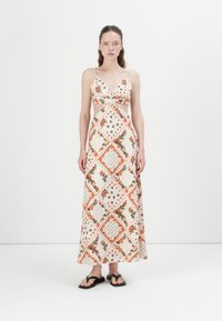 Maxi-jurk met een diagonaal bloemenpatroon in oranje en groen op een crèmekleurige achtergrond, met een uitsnijdesign en dunne verstelbare bandjes.