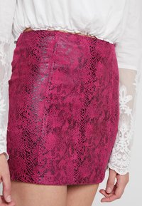 Mini falda de serpiente sintética en rosa brillante con un acabado brillante, que presenta una textura suave y un sutil detalle en negro.