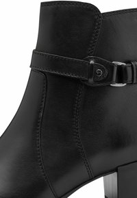 Melnas ādas potītes zābaki ar kvadrātveida papēdi, ar dekoratīvu siksniņu un metāla sprādzi, kā arī izstrādātu šuvju. Gluda tekstūra un elegants dizains.