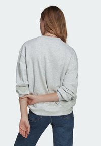 Ljusgrå sweatshirt med nedhasade axlar och uppvikta ärmar, tillverkad av mjukt tyg, kombinerad med mörkblå jeans och ett enkelt halsband.