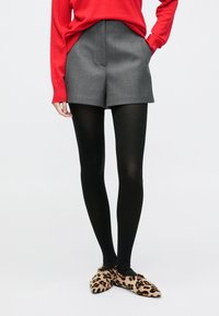 Pantalones cortos grises a medida con dos bolsillos laterales, combinados con medias negras y bailarinas de estampado de leopardo. El suéter es de color rojo brillante con tejido texturizado.