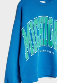 Sudadera azul con la palabra "MICHIGAN" en letras verdes bold con un contorno blanco, y "LAKES STATE" debajo, hecha de una tela suave y texturizada.