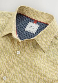 Camisa con cuello en amarillo con patrones geométricos blancos, con un interior de patrón azul marino, botones blancos y una etiqueta ajustada.