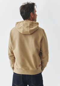 Sudadera color caqui con capucha con cordón, puños y dobladillo acanalados; material suave y una etiqueta beige en el lado inferior izquierdo.