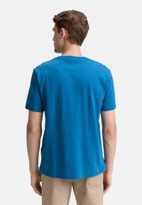 Kortærmet blå T-shirt med et struktureret, stribet mønster, der har en rund halsudskæring og en afslappet pasform på en person, der vender væk fra beskueren.