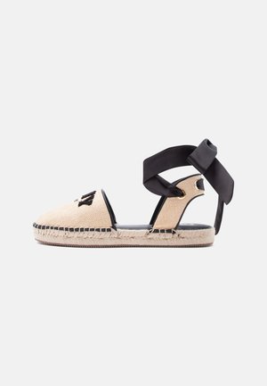 Μπεζ σανδάλι εσπαντρίγια με μαύρο κεντημένο λογότυπο, σόλα από γιούτα και μαύρο κορδόνι δέσιμο στον αστράγαλο σε λευκό φόντο.