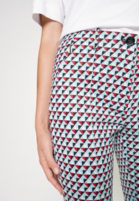 Spodnie w wysokim stanie w geometryczny wzór czerwonych, czarnych i jasnoniebieskich trójkątów. Posiadają zamek i zapięcie na guzik, dopasowany krój.