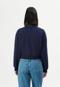 Cropped navy sweatshirt with long sleeves, elastic waistband, and ribbed cuffs, paired with high-waisted light blue denim jeans.