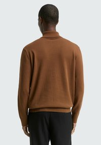 Pull en tricot marron avec un col montant, design ajusté, poignets et ourlet côtelés. Texture lisse, vu de dos sur un fond clair.