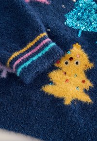 Granatowy, puszysty sweter z żółtym, puszystym motywem choinki z kolorowymi ozdobami oraz prążkowanymi mankietami w różowe, niebieskie i żółte paski.