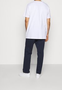 White cotton t-shirt, relaxed fit, paired with navy blue pants and white sneakers. Simple design, no visible patterns or accents.