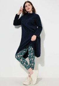 Tunika blu navy a maniche lunghe con colletto alto, abbinata a leggings verde a fiori e sneakers bianche chunky.
