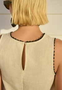 Linnen mouwloos jurk in lichtbeige met een geschulpte zwarte rand en details met een sleutelgat aan de achterkant, voorzien van een kleine knoopsluiting bij de nek.