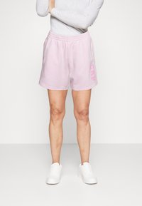 Shorts di cotone rosa con vita elastica e logo "GAP" in rosa chiaro sul lato, abbinati a scarpe da ginnastica bianche.