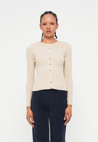 Beige pletený cardigan s kulatým výstřihem, dlouhými rukávy a předním zapínáním na knoflíky. Obsahuje jemnou strukturu a knoflíky ve stříbrném odstínu.