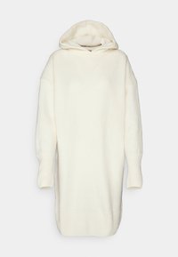 Longue robe à capuche tricotée couleur crème avec épaules tombantes et poignets et ourlet côtelés, présentée sur fond blanc uni.