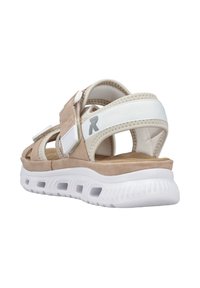 Sandales en suede beige avec des sangles élastiques blanches, fermetures ajustables à crochets et boucles, et une semelle blanche rembourrée comportant des découpes de ventilation.