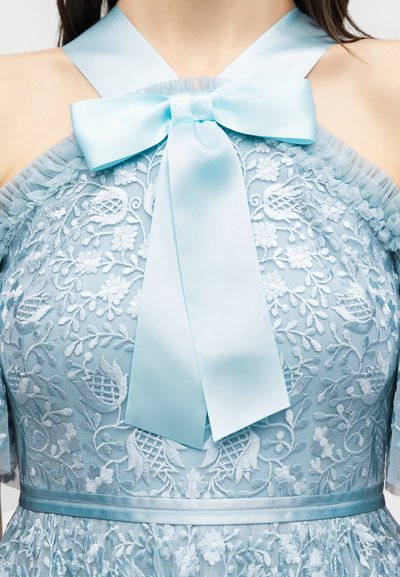 Φόρεμα από γαλάζια δαντέλα με λουλουδένια σχέδια, διαφανείς ραμμένες μανσέτες με βολάν και μεγάλο σατέν φιόγκο στο ντεκολτέ.
