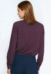 Bluzka z długim rękawem w ciemnym bordo z małymi jasnoróżowymi kropkami. Wykonana z gładkiej tkaniny, o klasycznym kroju i mankietach zapinanych na guziki.