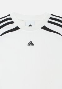 Λευκό αθλητικό μπλουζάκι με μαύρες οριζόντιες ρίγες στους ώμους, με κεντημένο μαύρο λογότυπο Adidas στο κέντρο. Μαλακή υφή.
