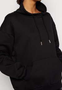 Sudadera negra hecha de un tejido suave con un alto cuello, cordones y un gran bolsillo frontal. Cuenta con puños y dobladillo acanalados.