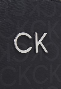 Materiale nero testurizzato con motivo a rilievo del logo CK. Lettere "C" e "K" in argento lucido come accentuazioni.