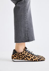Zapatillas con estampado de leopardo y parte superior texturizada, detalles en cuero negro, cordones blancos y suela de goma, combinadas con jeans cortos grises.